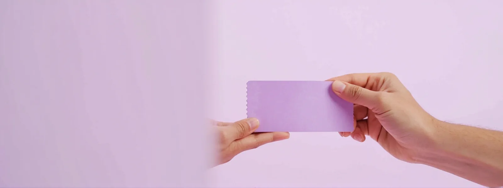 Wide editorial banner of a hand passing a violet ticket stub to another hand